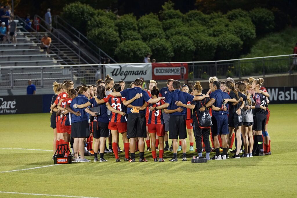 Female soccer plays in huddle with transformational coach, not a fear-based coach.